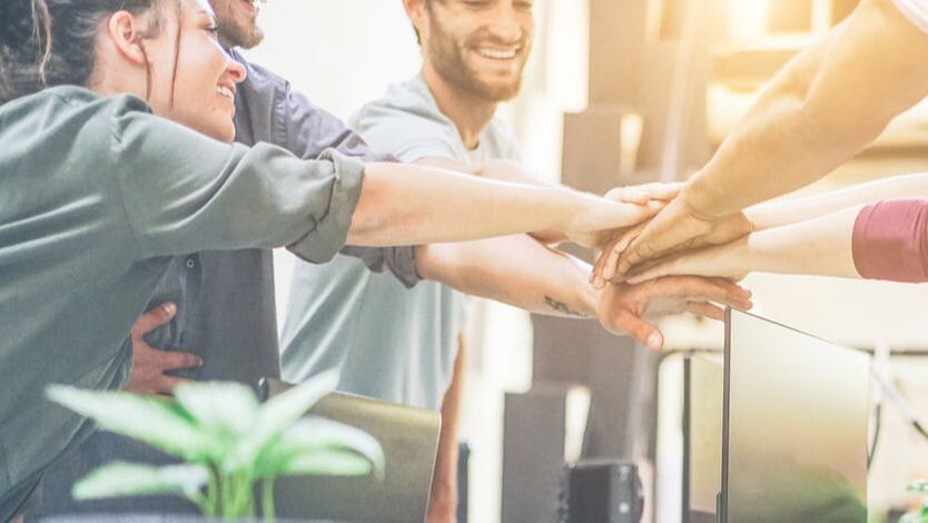 People with hands stacked together, smiling, showing teamwork.