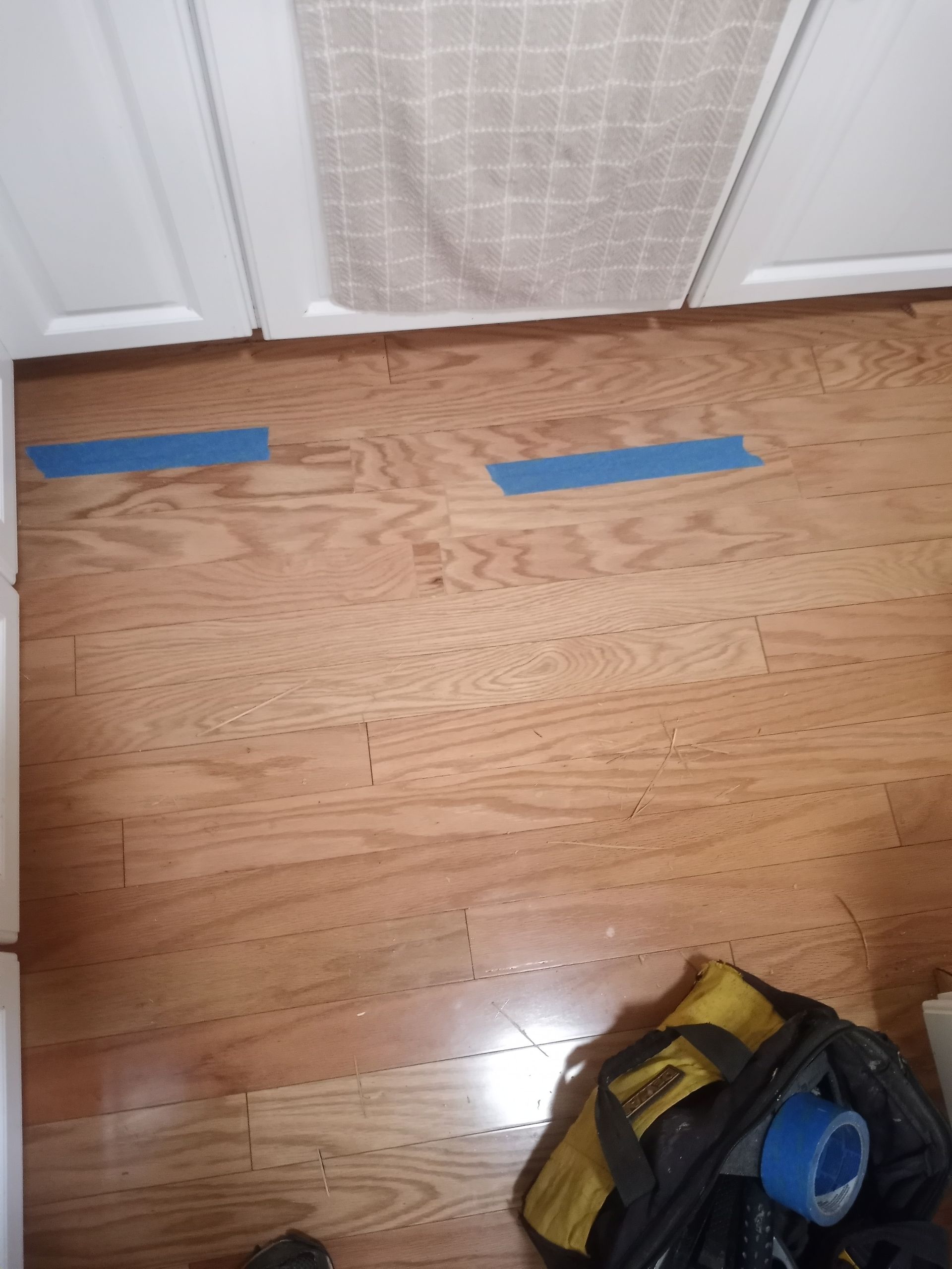 A wooden floor with blue tape on it and a bag on the floor.