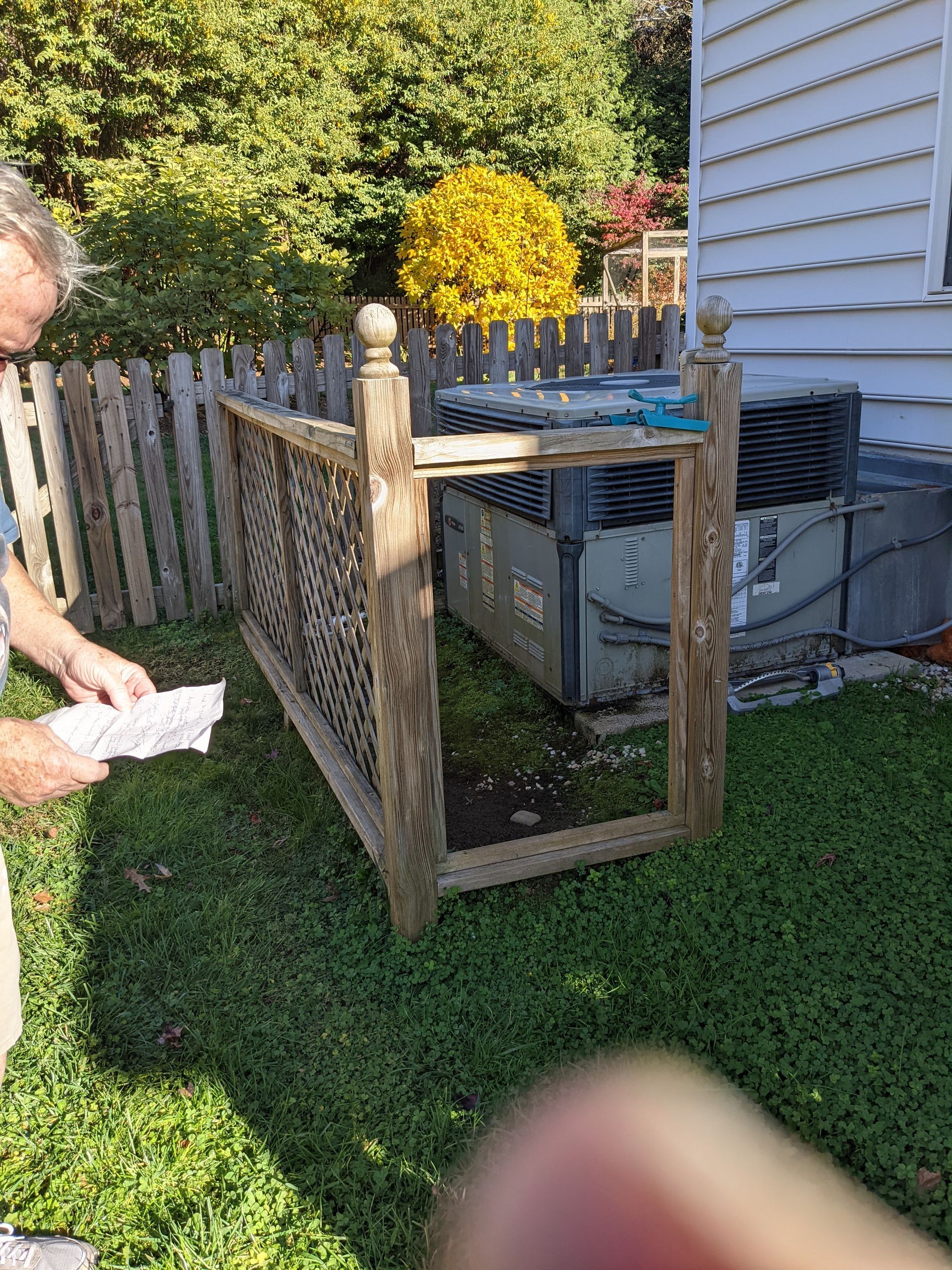 A man is standing next to a wooden fence in a backyard.