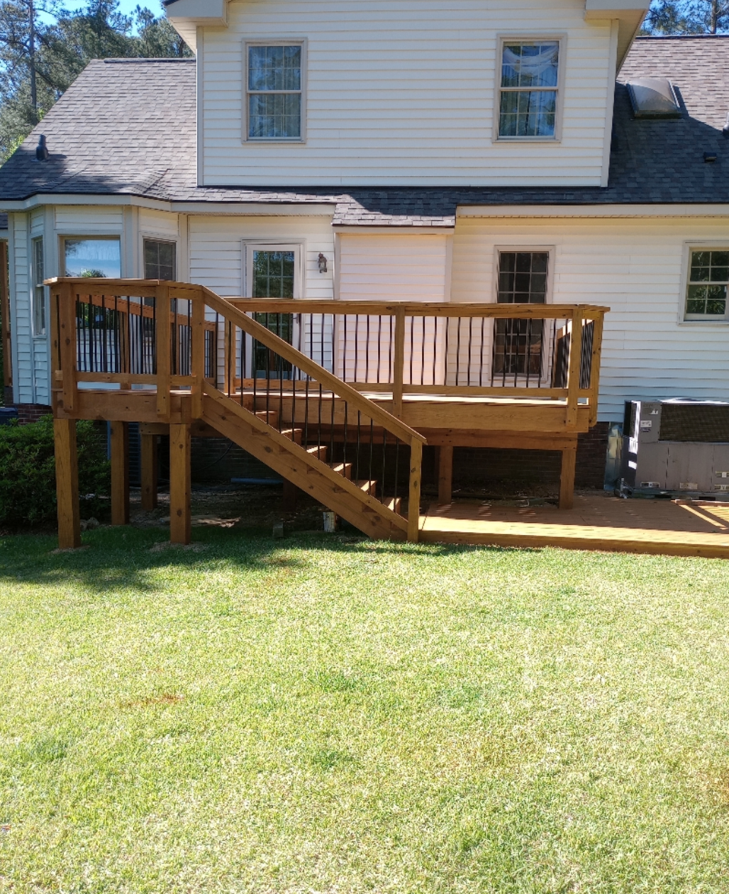 A wooden deck with stairs leading up to it is in the backyard of a house.