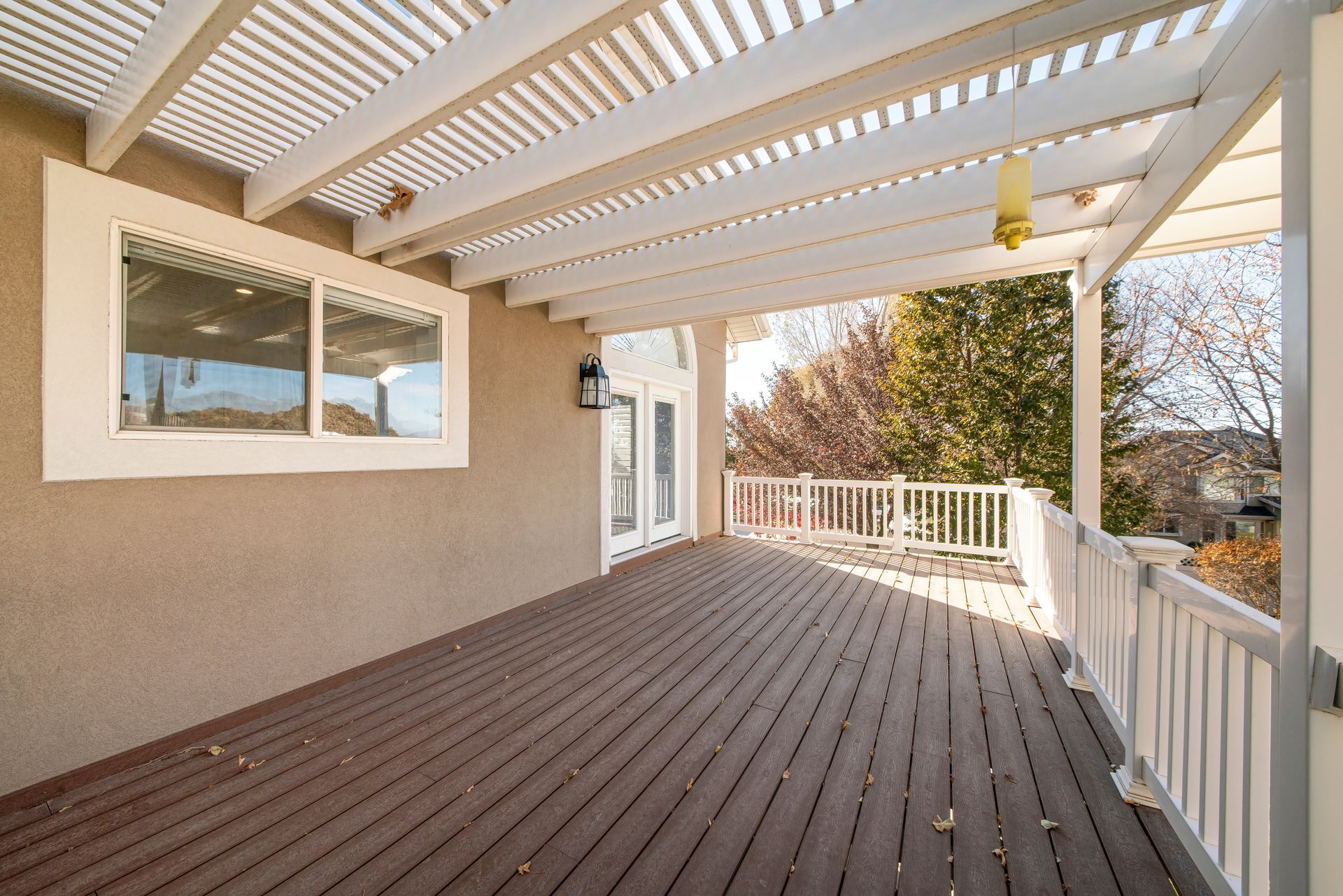 An empty deck with a pergola and a white railing.