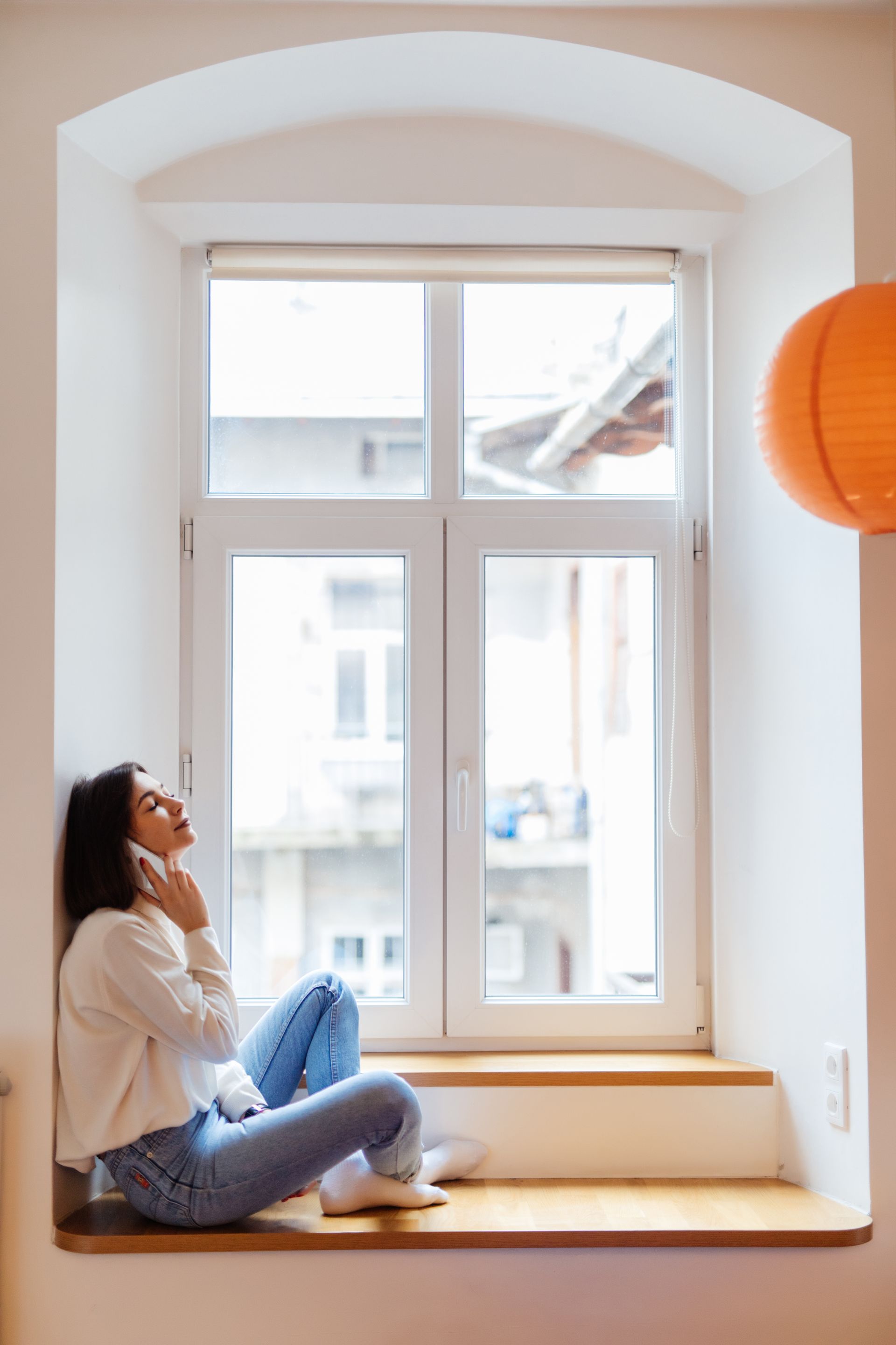 A woman is sitting on a window sill talking on a cell phone.