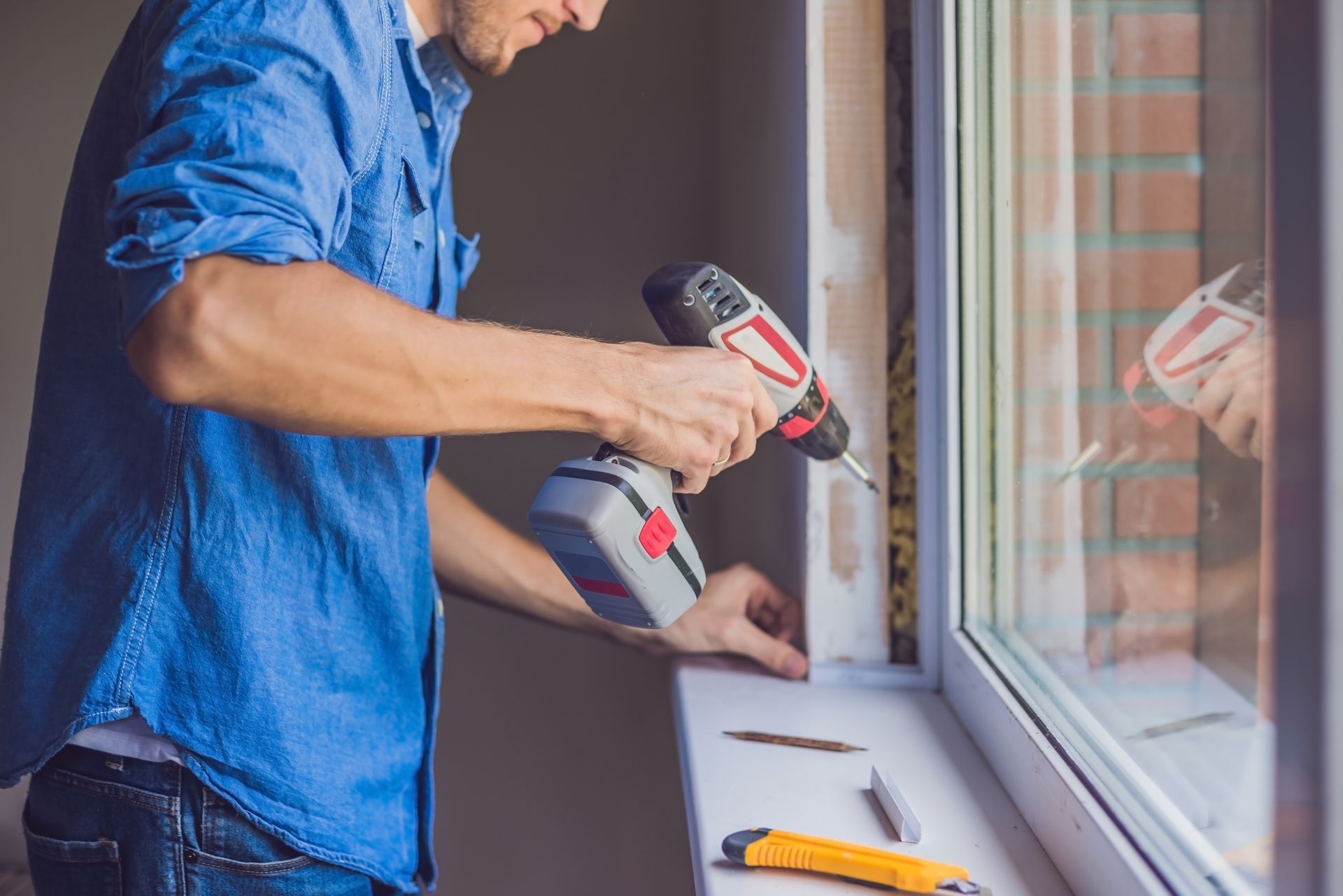 A man is installing a window sill with a drill.