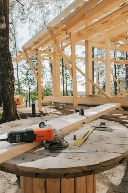 A grinder is sitting on a wooden table in front of a wooden structure under construction.