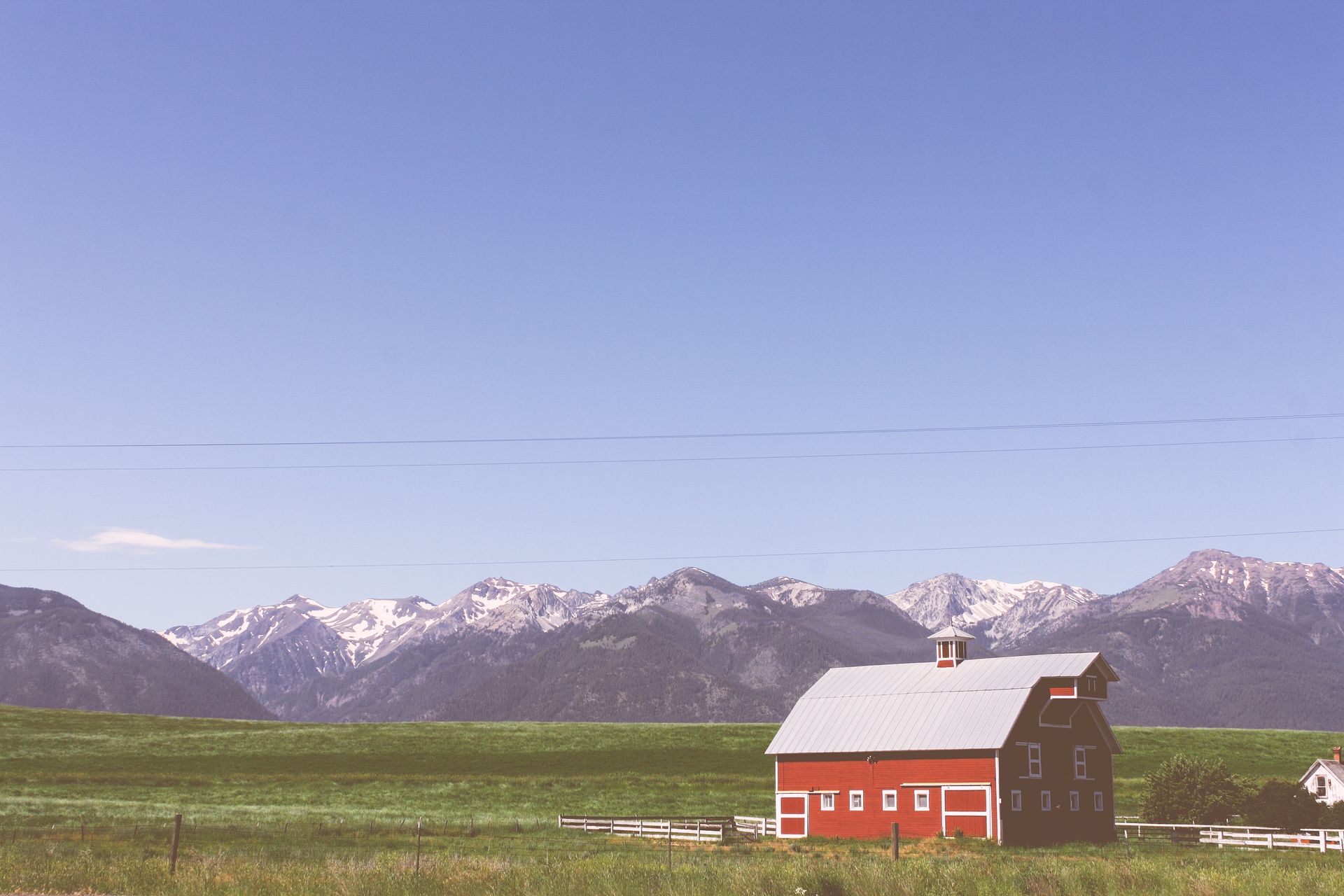 A red barn is sitting in the middle of a grassy field with mountains in the background.