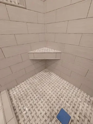 Empty tiled shower with a corner shelf. White and gray tiles.