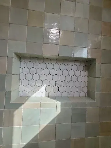Shower wall with recessed shelf. The main wall is pale green tile, the shelf interior is white hexagon tile.