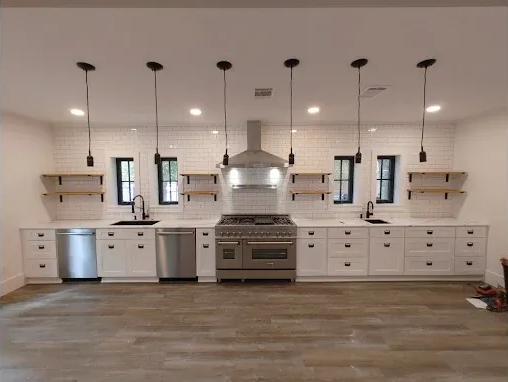 Modern white kitchen with stainless steel appliances, black accents, and pendant lights.