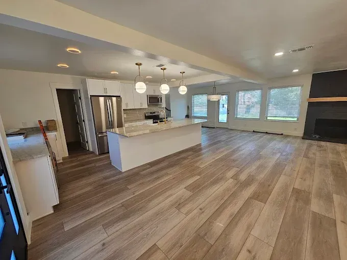Spacious, bright kitchen with white cabinets, island, and stainless steel appliances.  Wooden floor, windows, and fireplace.