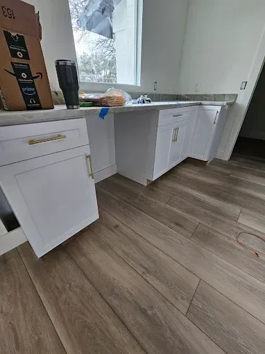 White kitchen cabinets with gold hardware. Wood-look floor and a window above the countertop.