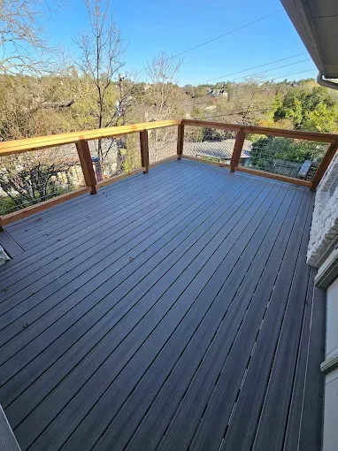 Gray composite deck with wood railing, overlooking a tree-filled landscape under a blue sky.