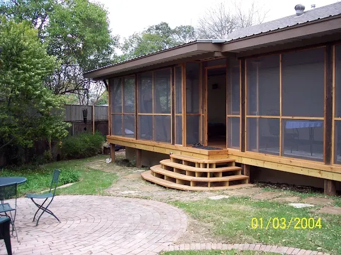 Screened porch with wooden steps, brick patio, grass, and trees.