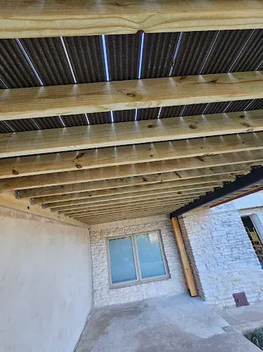 Wooden beams and corrugated metal roofing cover a porch. A window is visible.