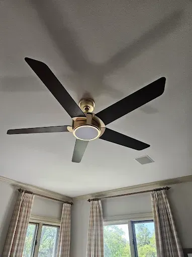 Ceiling fan with dark brown blades, gold accents, and a built-in light, casts shadow on white ceiling.