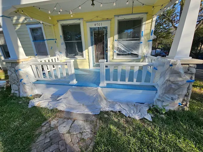 House porch being painted blue and white, windows and surrounding area covered in plastic.