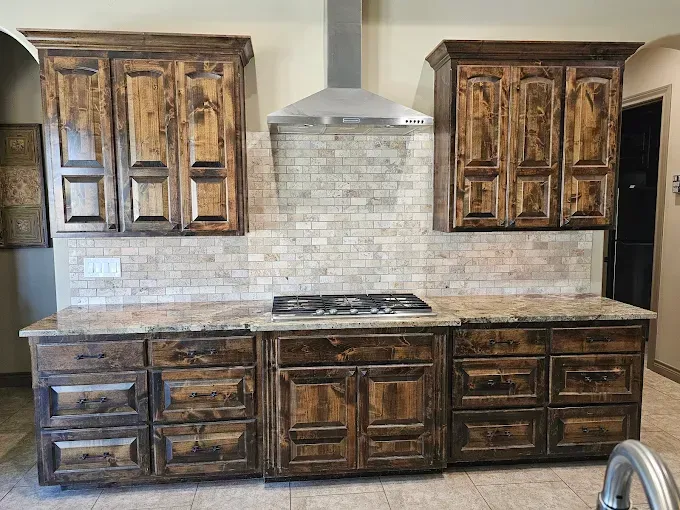 Kitchen with brown wooden cabinets, beige backsplash, granite countertops, and a stainless steel range hood.