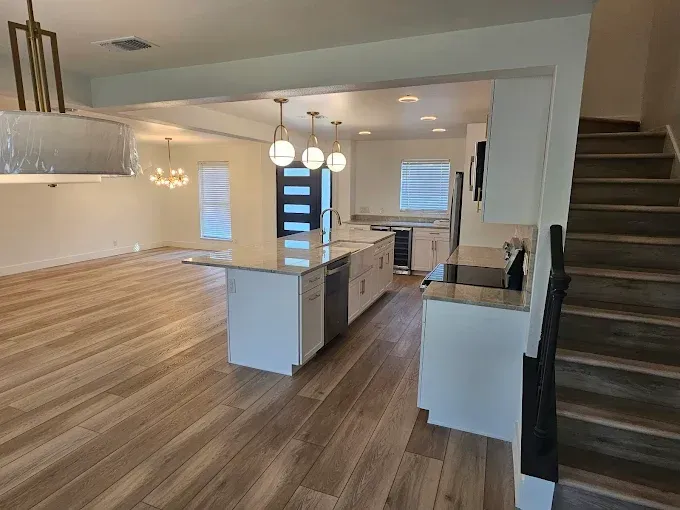 Interior view of a modern home with a kitchen, stairs, and living area with wood-look flooring.