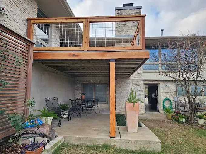 Wooden deck with metal railing above a patio with outdoor furniture, in a backyard.