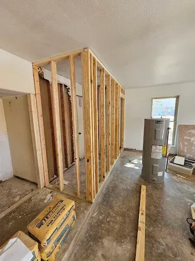 Interior view of a room under construction. Stud framing for a wall and door. Cement bags on the floor.