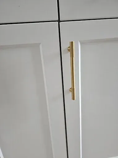 White cabinet doors with a vertical gold bar handle.