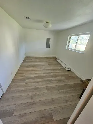 Empty room with wood-look flooring, white walls, a window, and a ceiling light.