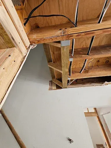 Interior view showing exposed wooden framing of a ceiling/attic, with electrical wires and a section of wall.
