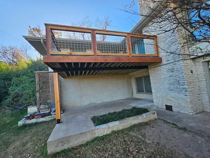 A wooden deck built onto a two-story brick home with a concrete patio below.