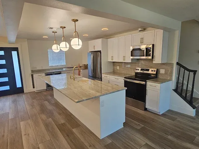 Modern kitchen with white cabinets, island, stainless steel appliances, and wooden floors.