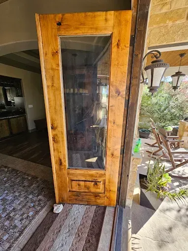 Wooden door with glass panel, stained brown, leaning on a porch step.