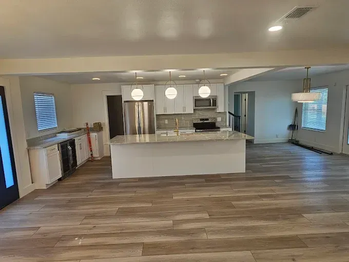 Newly renovated kitchen with white cabinets, island, stainless steel appliances, and wood-look flooring.
