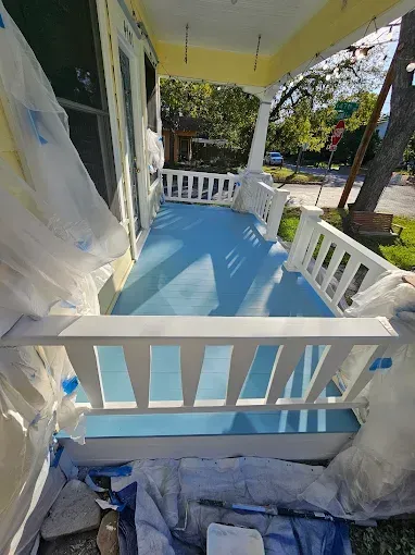 Newly painted blue porch with white railings on a yellow house; covered in protective tarps.