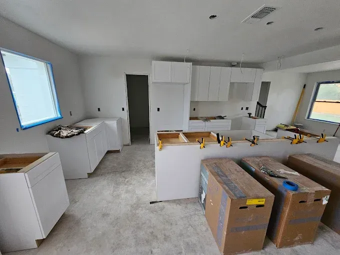 Kitchen under construction with white cabinets, boxes, and tools.