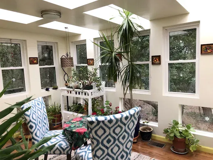 Sunroom with plants, skylights, patterned chairs, and white walls.