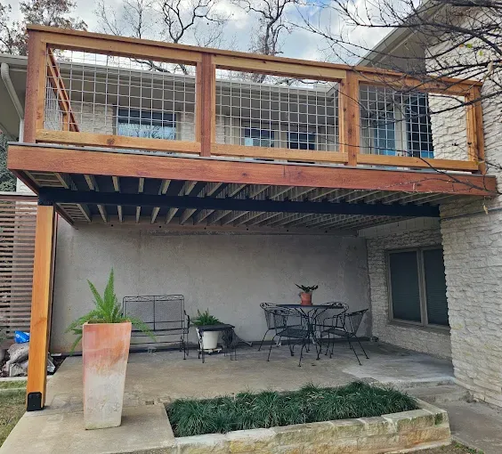Wooden deck with metal railing overlooking a patio with furniture and plants.