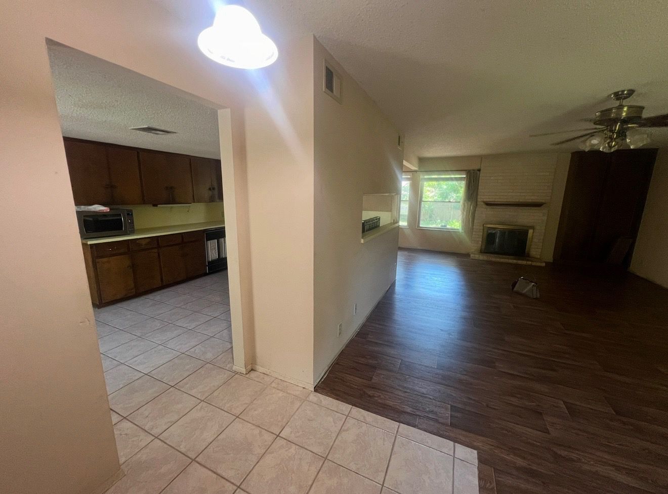 A hallway with tile floor leads to a kitchen and living room with dark wood floors.