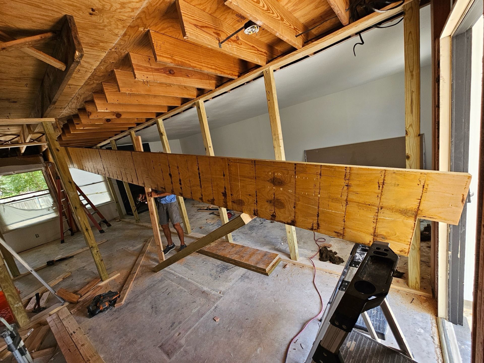 Interior construction: wooden beams, framing, and supports in a room with exposed ceiling and person working.