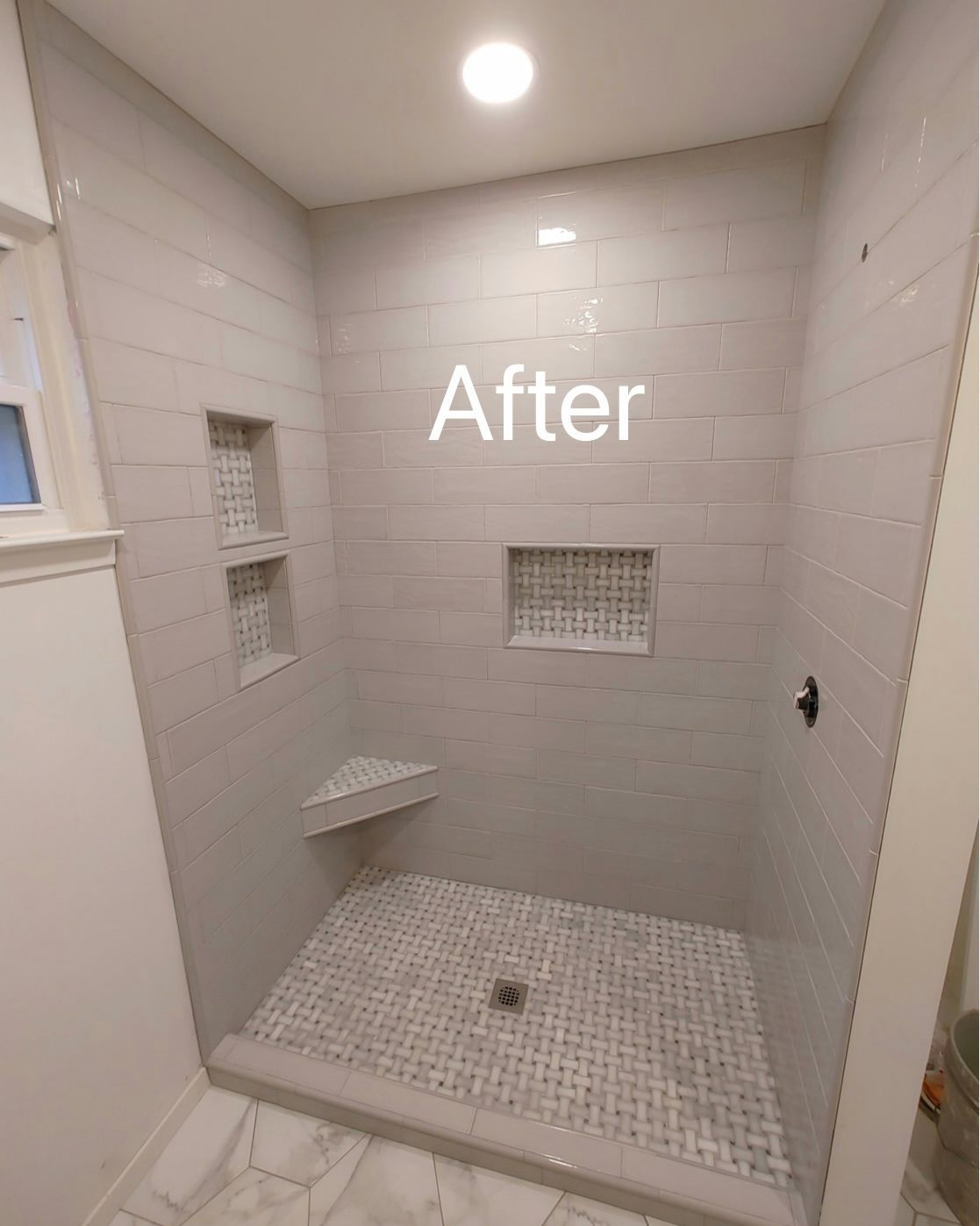 Newly tiled, light gray shower with mosaic floor, recessed shelves, and corner seat.