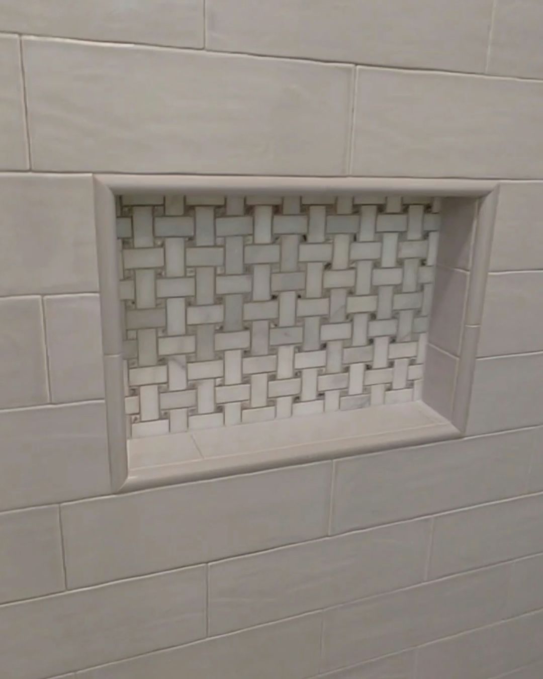 Recessed shower niche with woven mosaic tile backing, surrounded by beige rectangular tiles.