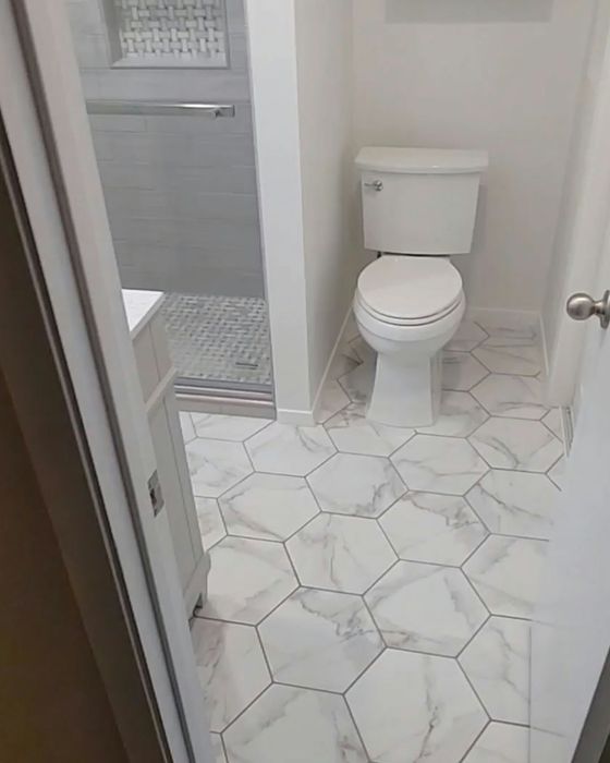 White bathroom with hexagonal marble-look floor tiles, white toilet, and glass shower door.