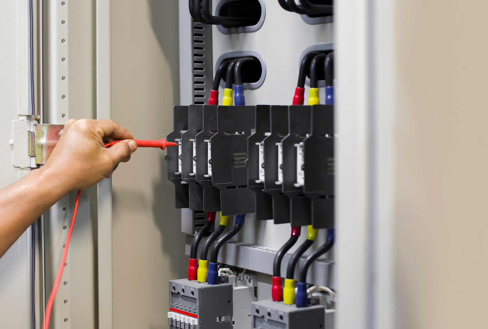 Person testing electrical wires in a panel with a multimeter. Black, blue, and yellow wires visible.