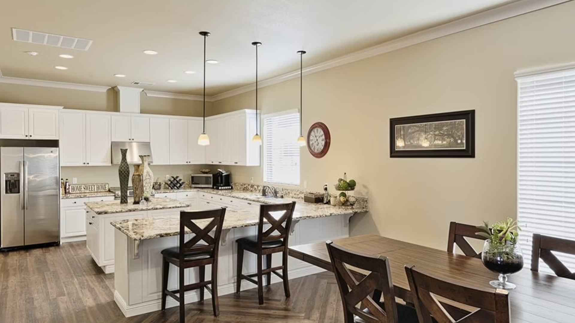 Kitchen with white cabinets, granite countertops, island with bar stools, and dining table.