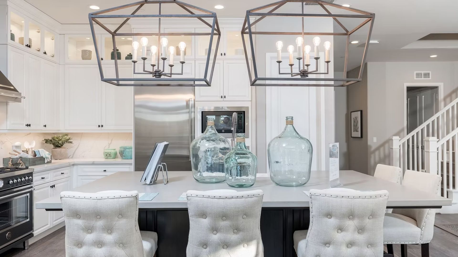 Elegant kitchen with island seating, glass decor, and geometric chandeliers.
