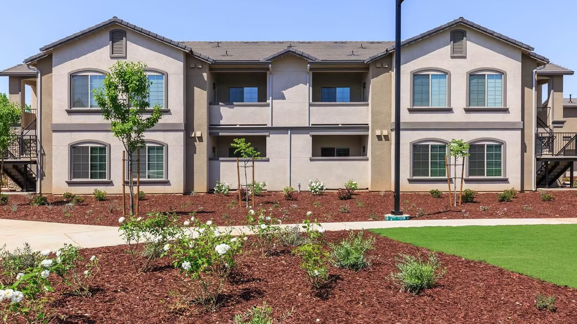 Two-story beige apartment building with brown mulch landscaping and green grass lawn.
