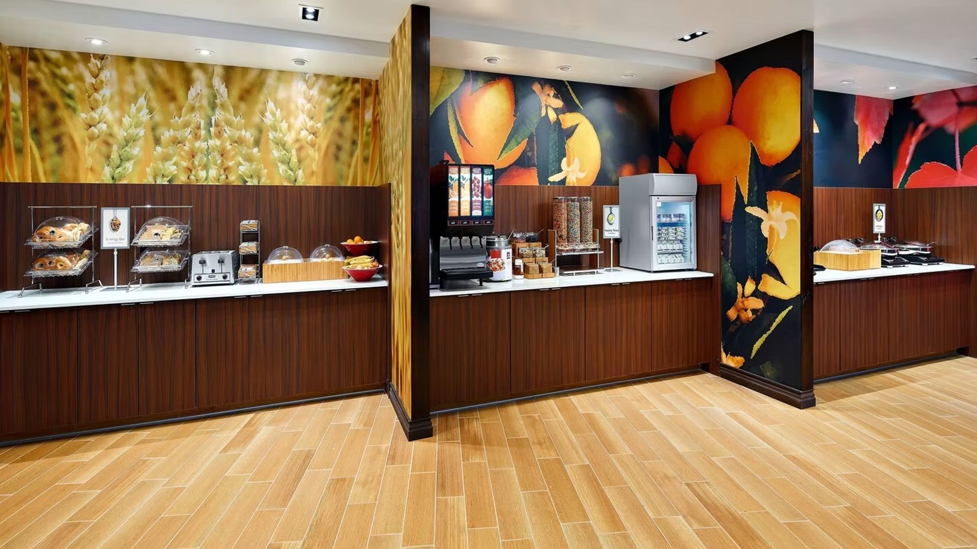 Hotel breakfast buffet with pastries, cereals, juice dispensers, and vibrant wall art.