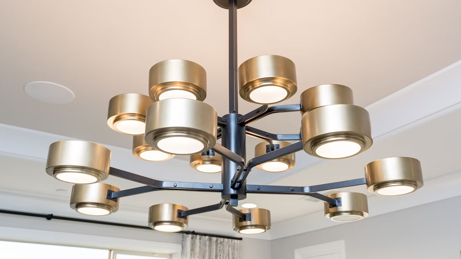 Gold and black modern chandelier with cylindrical light fixtures against a white ceiling.