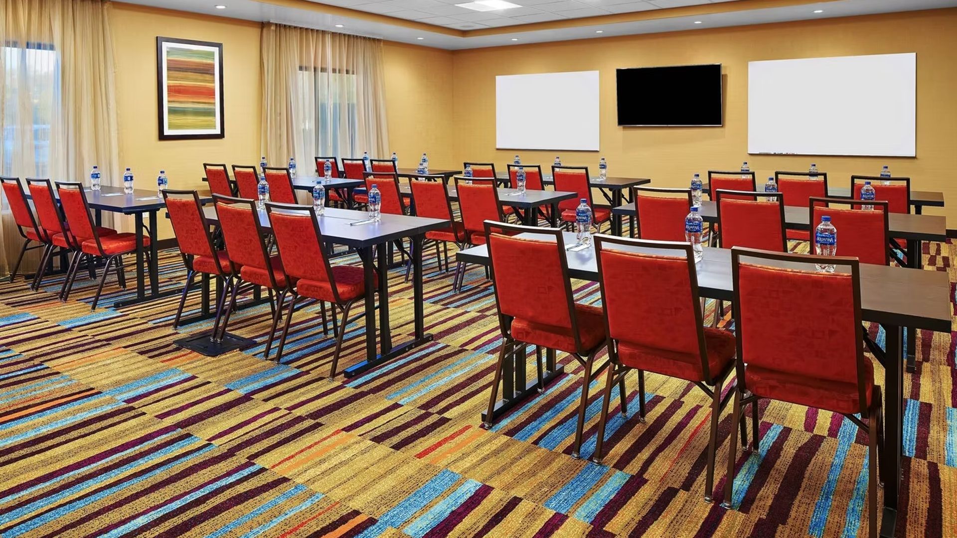 Conference room with red chairs, tables, whiteboards, TV, and colorful carpet.