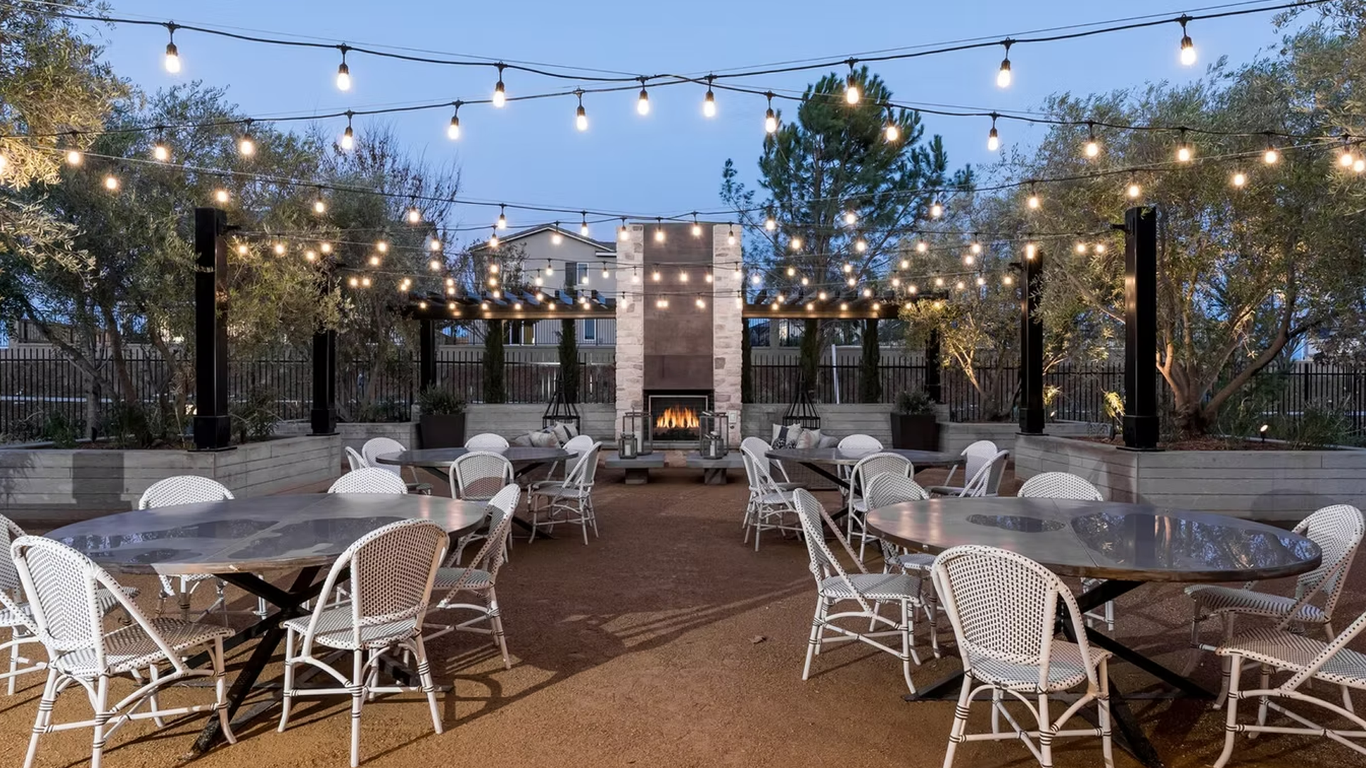 Outdoor dining area with string lights, tables, chairs, and a fireplace.
