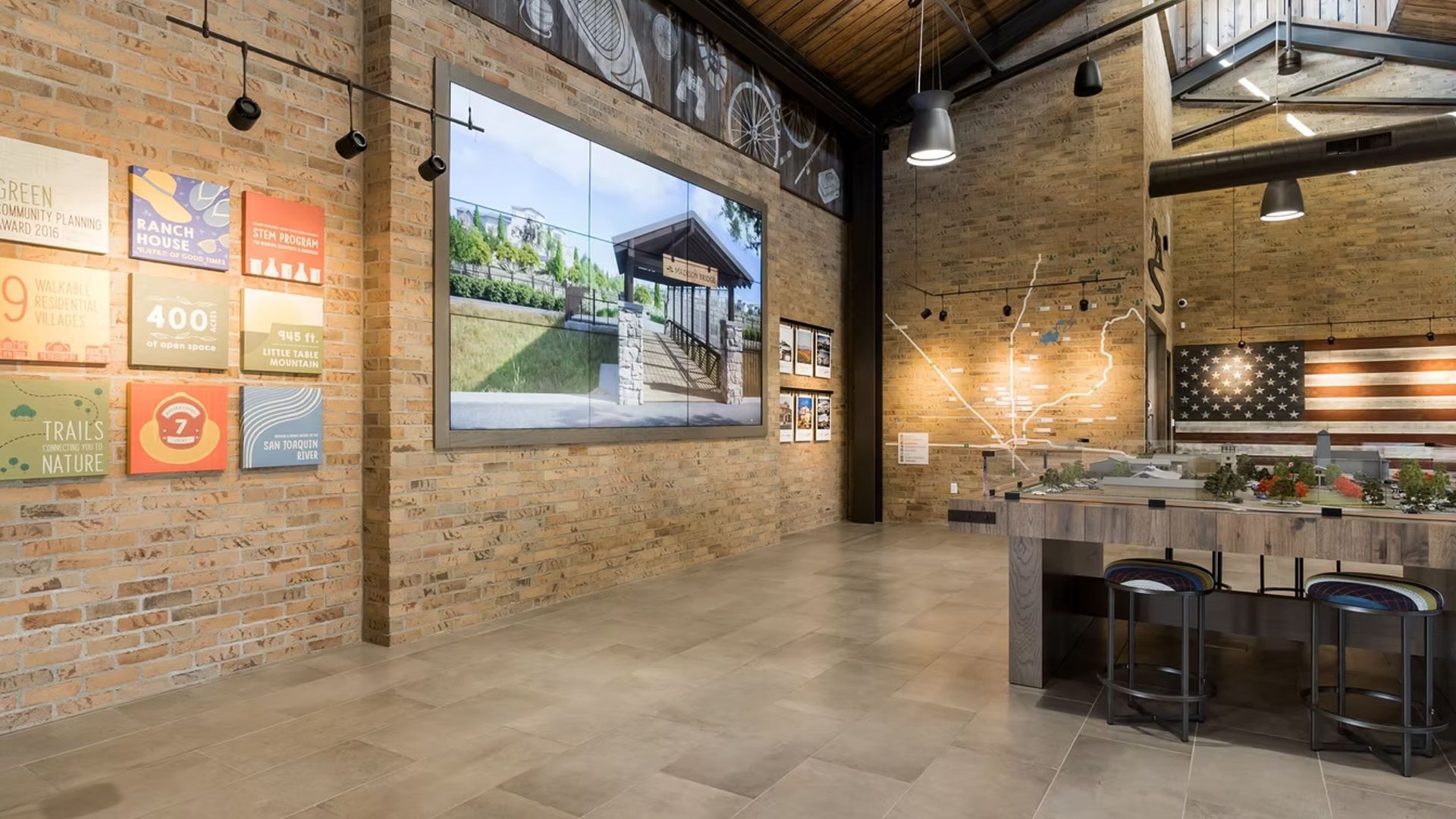 Interior view of a brick-walled room with a large screen, artwork, and a bar area with stools.