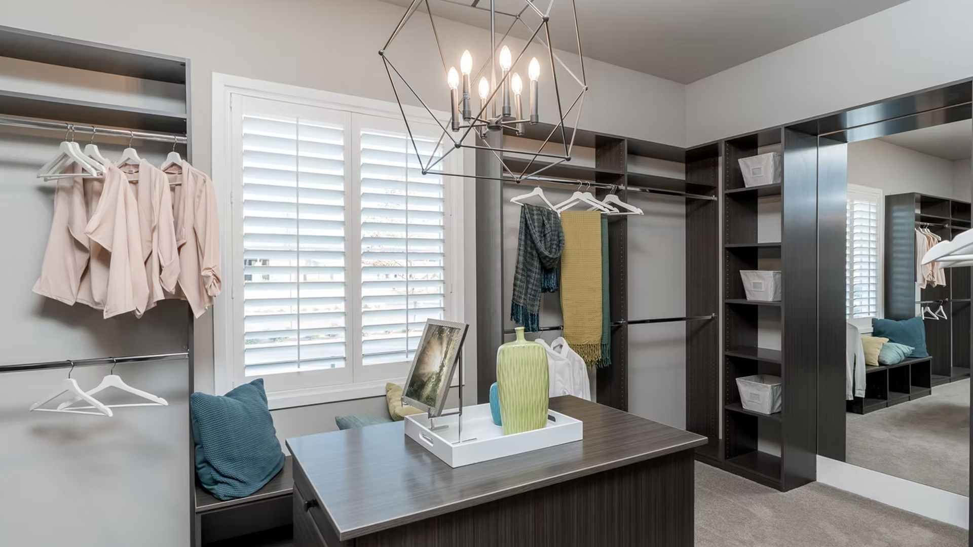 Walk-in closet with dark shelves, white clothing, central vanity table, and large mirror.
