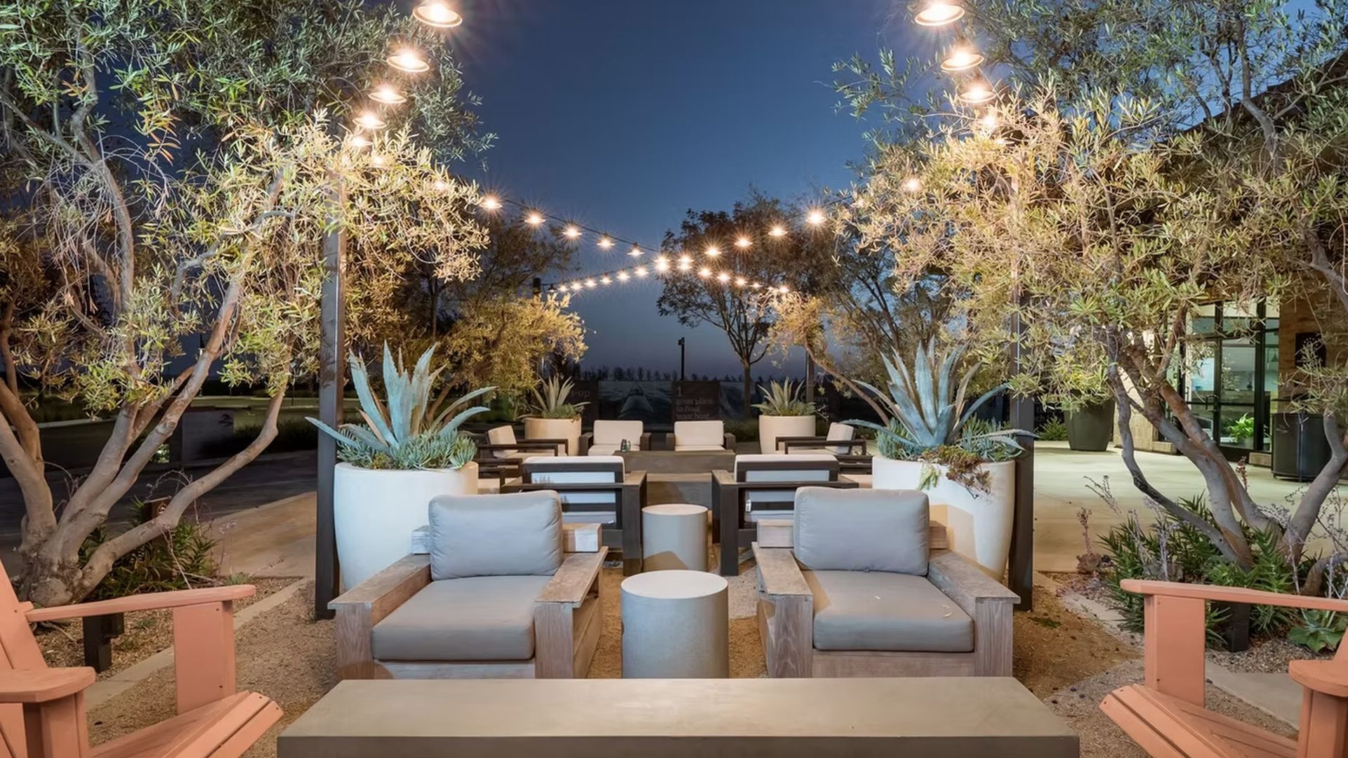 Outdoor seating area with string lights, trees, and gray cushioned furniture.